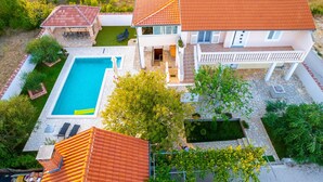 A two-story house with a swimming pool, a patio with outdoor furniture, and a garden.
