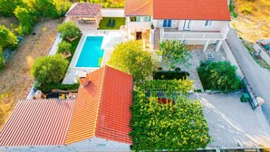 A two-story house with a swimming pool, a covered patio, and a garden.
