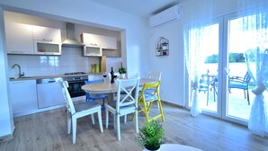 A modern kitchen with white cabinets, a dining area with a round table and chairs, and a view through large glass doors to an outdoor patio.