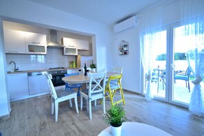 A modern kitchen with white cabinets, a dining area with a round table and chairs, and a view through large glass doors to an outdoor patio. - Holiday Home Dinko with pool (Pridraga)