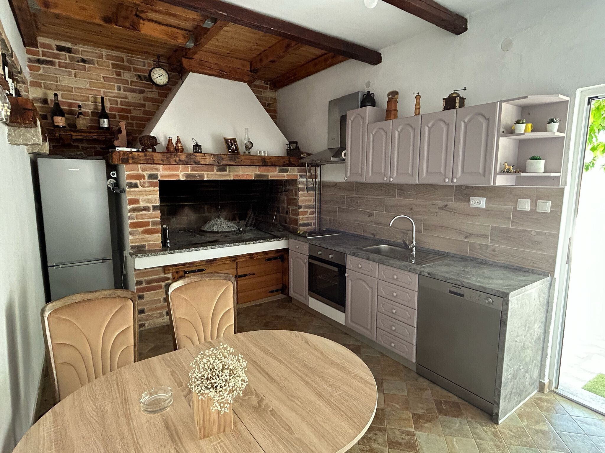 A kitchen with a brick oven, wooden chairs, a dining table, and a sink.