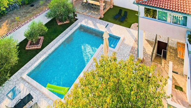 A pool with a patio, a covered seating area, and a view of a lush landscape.