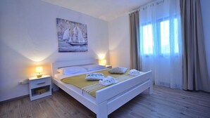 A bedroom with a bed, nightstands, a painting, and a window with curtains.