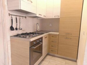 Eine kleine Küche mit Gaskochfeld, Backofen und Spüle. Es gibt Holzschränke mit silbernen Griffen und eine geflieste Spritzschutzwand.