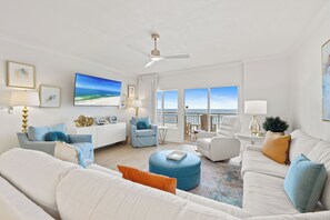A spacious living room with a large TV, multiple seating areas, and a balcony with a view. - Admiral's Quarters 906 by Liquid Life (Orange Beach)