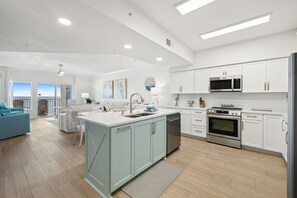 A modern kitchen with white cabinets, stainless steel appliances, and a large island. - Admiral's Quarters 906 by Liquid Life (Orange Beach)