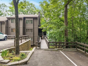 A multi-story building with a covered walkway leading to a parking area, surrounded by trees. - Lakefront Tree House | Big Canoe Mountain Getaway (Jasper)