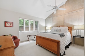 Une chambre à coucher avec un lit en bois, un ventilateur de plafond, une fenêtre avec des stores, une table de chevet et une commode.