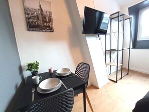 A dining area with a table set for two, a black chair, a small potted plant, and a flat-screen TV mounted on the wall. - Agr Able s Jour au Londres vue Sans Vis- -vis (Roubaix)