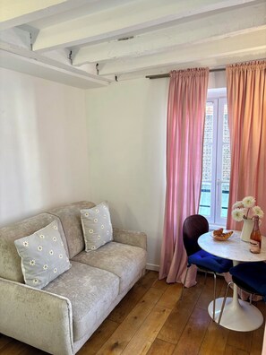 Ein gemütliches Wohnzimmer mit einer Couch, einem Tisch mit einer Vase und einer Flasche, und Blick durch rosa Vorhänge.