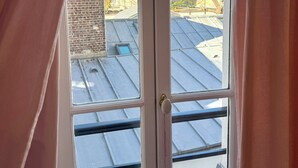 Ein Fenster mit Blick auf ein Gebäudedach und angrenzende Bauten.