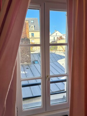 Ein Fenster mit Blick auf ein Gebäudedach und angrenzende Bauten.