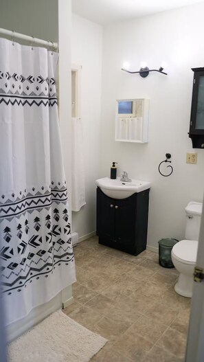 A bathroom with a shower curtain, a sink, a toilet, and a small window.