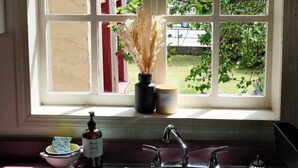 Una cocina con un lavamanos doble, una ventana con vistas a la vegetación y un florero con plantas secas en el alféizar.