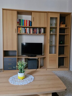 A room with a wooden TV stand, a flat-screen TV, a bookshelf, and a small table with a plant. - Eselei – Entire Holiday Apartment with Private Entrance (Belm)