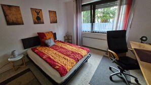 Una habitación de hotel con cama, escritorio, silla, radiador y ventana con cortinas.