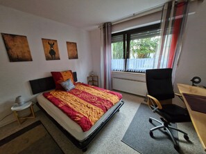 A hotel room with a bed, a desk, a chair, a radiator, and a window with curtains. - Eselei – Entire Holiday Apartment with Private Entrance (Belm)