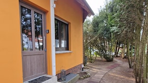 Un edificio con fachada amarilla, puerta de madera y un pequeño espacio al aire libre con una mesa y escalones que llevan a la entrada.