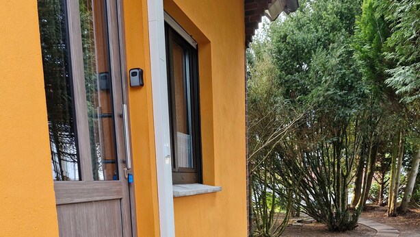 Un edificio amarillo con puerta de madera, una pequeña mesa exterior y un escalón de hormigón que lleva a la entrada.