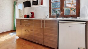 A kitchen with a microwave, toaster, and refrigerator, wooden cabinets, and a window with a view. - Holiday Home “Camping Les Pialades - Gîte Spa” with Private Terrace and Wi-Fi (Nabirat)