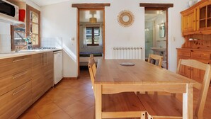 A kitchen with wooden cabinets, a dining table, and chairs. There is a window with curtains, a radiator, and a sunburst decoration on the wall. - Holiday Home “Camping Les Pialades - Gîte Spa” with Private Terrace and Wi-Fi (Nabirat)