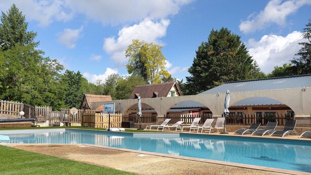 A swimming pool with lounge chairs, a wooden fence, and a building with a sloped roof in the background. - Holiday Home “Camping Les Pialades - Gîte Spa” with Private Terrace and Wi-Fi (Nabirat)