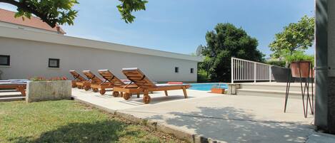 A poolside area with lounge chairs, a concrete deck, and a building with a white facade.