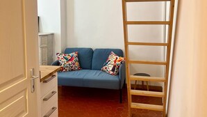 Ein Zimmer mit einem blauen Sofa, bunten Kissen, einer Holzleiter und einem weißen Schrank.