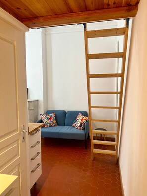 Ein Zimmer mit einem blauen Sofa, bunten Kissen, einer Holzleiter und einem weißen Schrank.