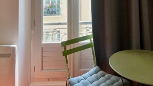 Ein Zimmer mit Blick auf Gebäude durch ein Fenster, ein Stuhl und ein Tisch.