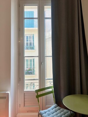 Ein Zimmer mit Blick auf Gebäude durch ein Fenster, ein Stuhl und ein Tisch.