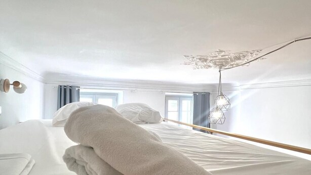 Ein Hotelzimmer mit einem ordentlich bezogenen Bett, einer Hängelampe und einem Fenster mit Vorhängen.