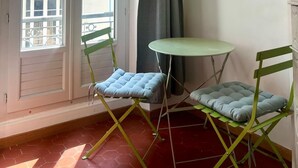 Ein Balkon mit zwei grünen Klappstühlen, einem kleinen runden Tisch und einem grauen Vorhang.
