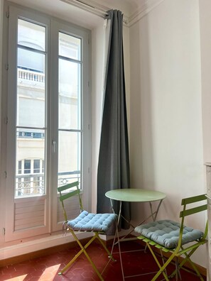 Ein Balkon mit zwei grünen Klappstühlen, einem kleinen runden Tisch und einem grauen Vorhang.