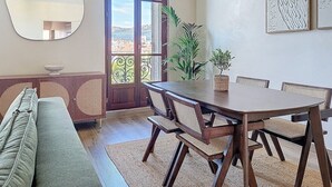 Uma área de refeições com uma mesa e cadeiras de madeira, um espelho redondo e vista através de uma porta de vidro.