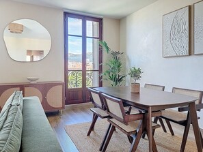 A dining area with a wooden table and chairs, a round mirror, and a view through a glass door. - L'Anatole - superb harbor view, hypercentre & cosy (Toulon)