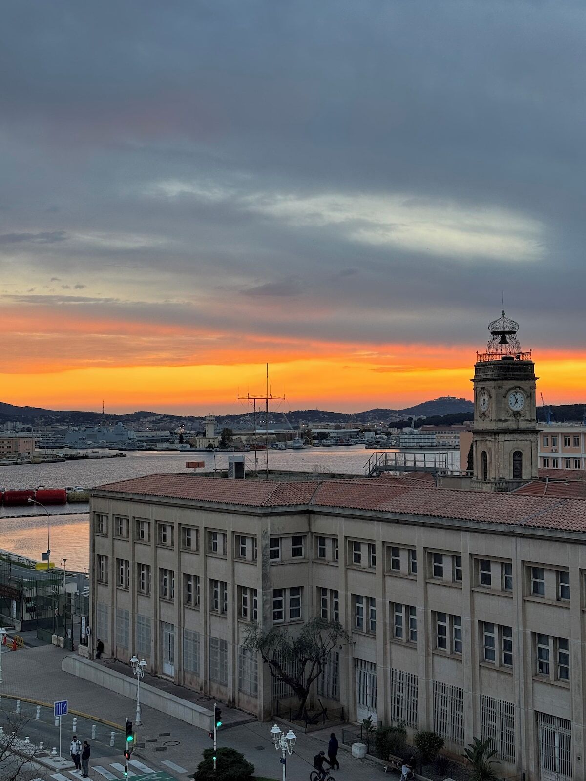 A building with a clock tower, a waterfront view, and a sunset.
