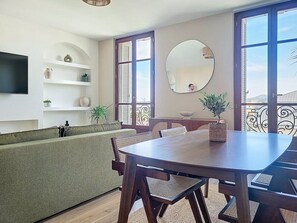 A dining area with a wooden table and chairs, a green sofa, a TV mounted on the wall, and a balcony with a view. - L'Anatole - superb harbor view, hypercentre & cosy (Toulon)