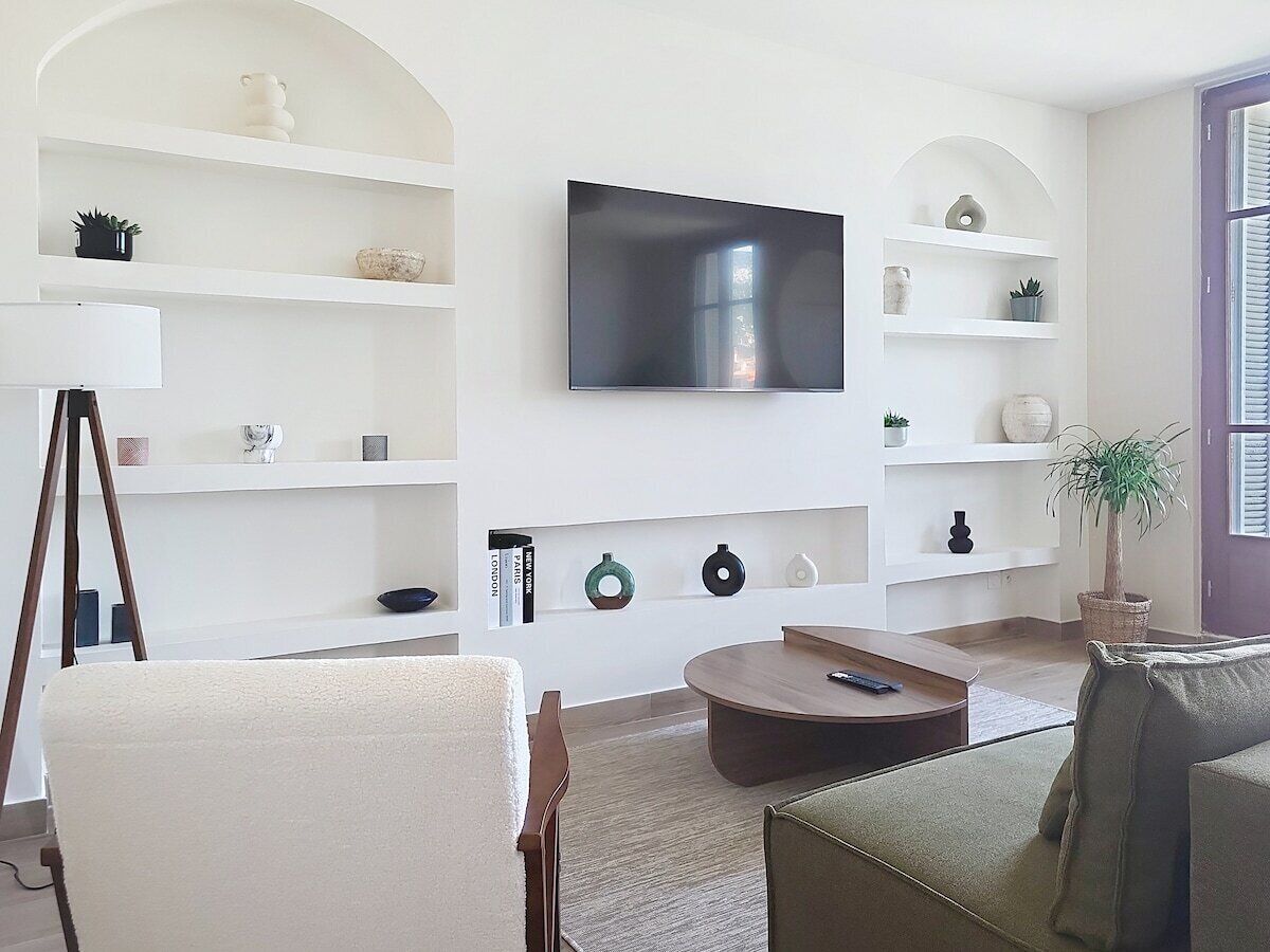 Una sala de estar con televisor de pantalla plana, estanterías blancas, una mesa redonda de centro y un sofá.