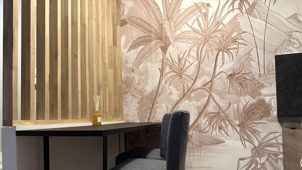 A room with a wooden slatted partition, a chair, and a wall with a tropical plant mural. - Comfortable apartment in the heart of the city (Toulon)