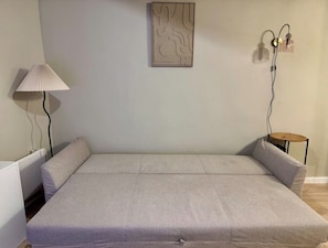 Ein Zimmer mit Bett, Lampe, Wandbild und einem kleinen Tisch mit Stuhl.