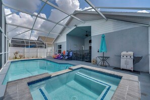 Ein Schwimmbecken mit überdachtem Patio, Deckenventilator und Grill.