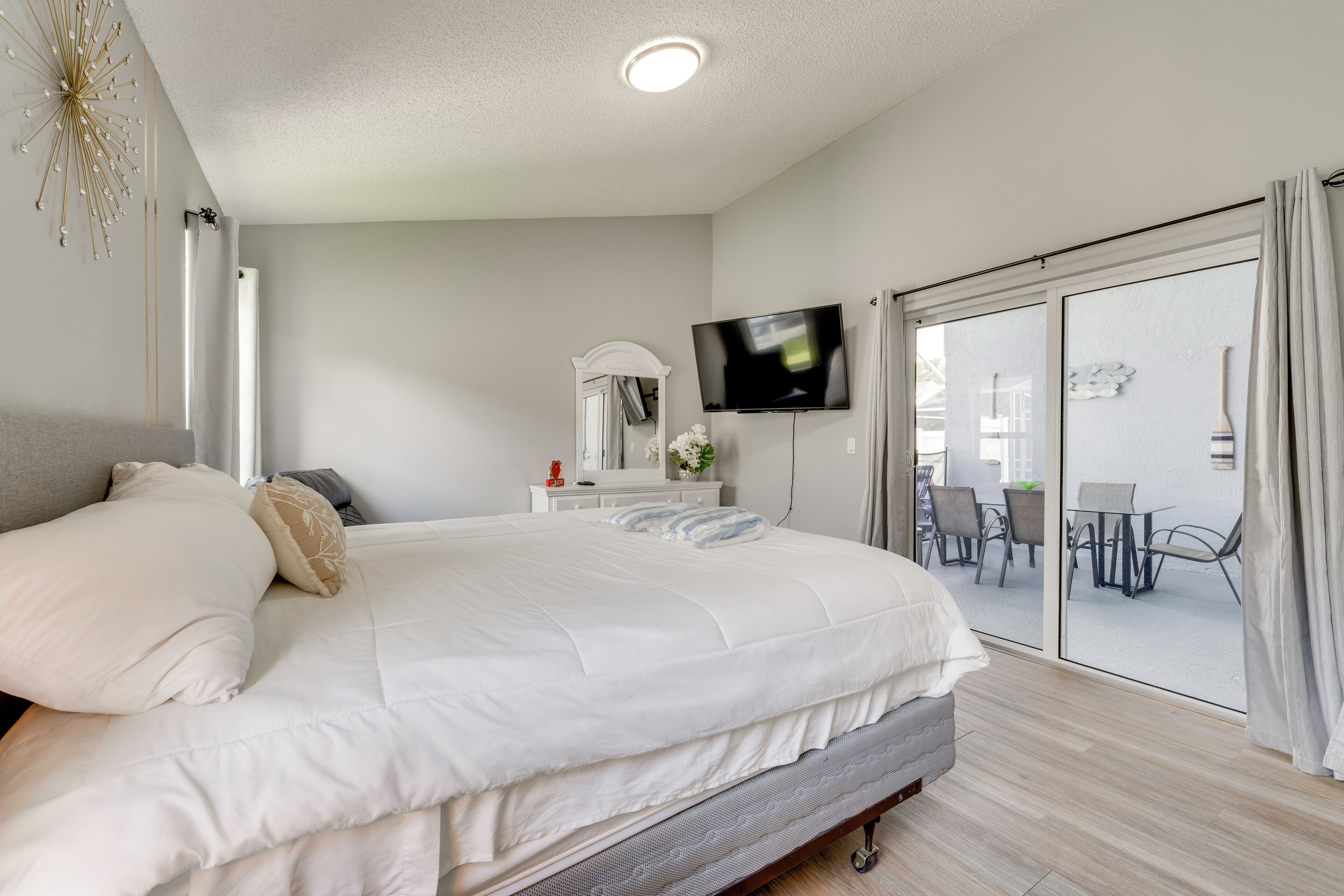 A bedroom with a large bed, a TV, a sliding glass door to a balcony, and a white dresser.