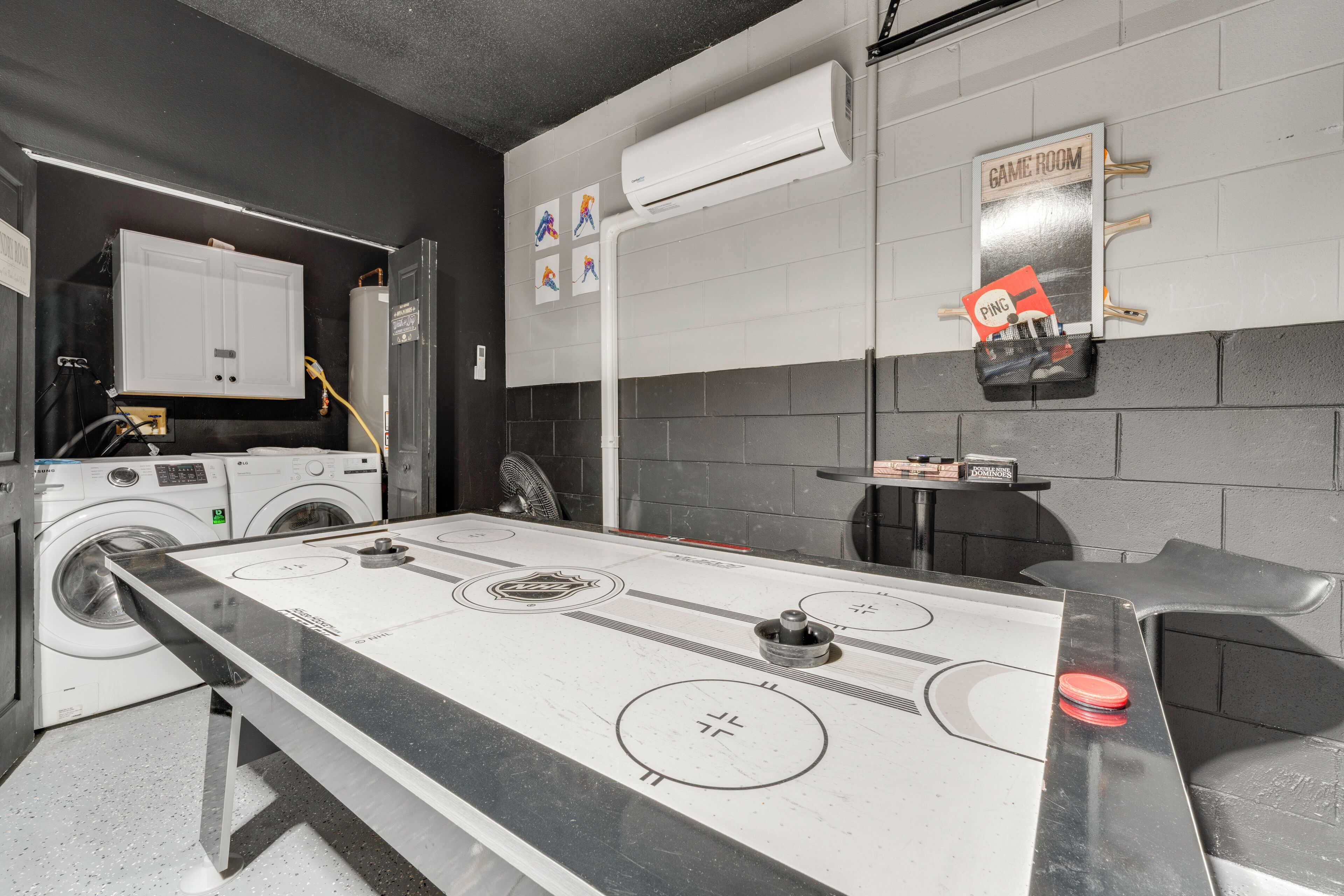 A room with a shuffleboard table, a laundry area with washers and dryers, and a sign indicating a game room.