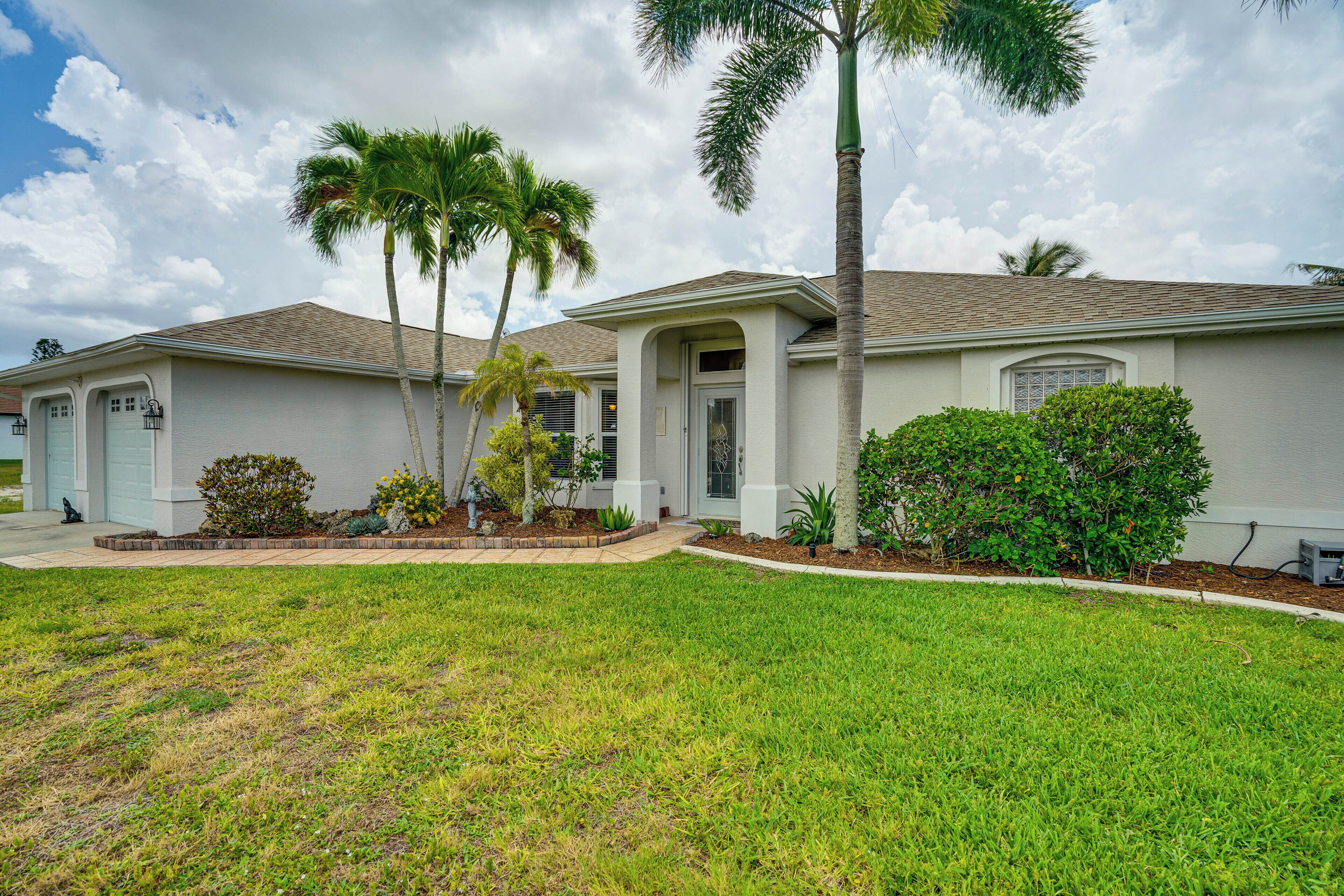 A residential house with a front lawn, palm trees, and a well-maintained garden.