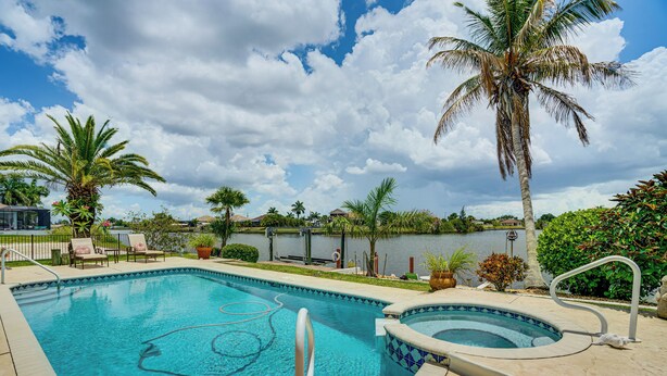 A swimming pool with a hot tub, surrounded by palm trees and a view of a body of water. - Spectacular Views! Largest Canal in NW Cape Coral (Cape Coral)