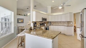 A kitchen with white cabinets, a granite countertop, a ceiling fan, and a refrigerator. - Spectacular Views! Largest Canal in NW Cape Coral (Cape Coral)