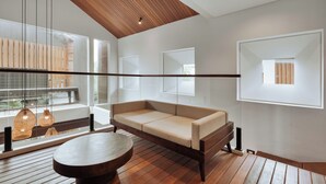 A modern interior with a wooden ceiling, a sofa, a round table, and large windows. - Aluna Ubud Villas (Ubud)