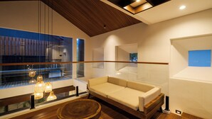 A modern interior with a wooden ceiling, a sofa, a round wooden table, and pendant lighting. - Aluna Ubud Villas (Ubud)