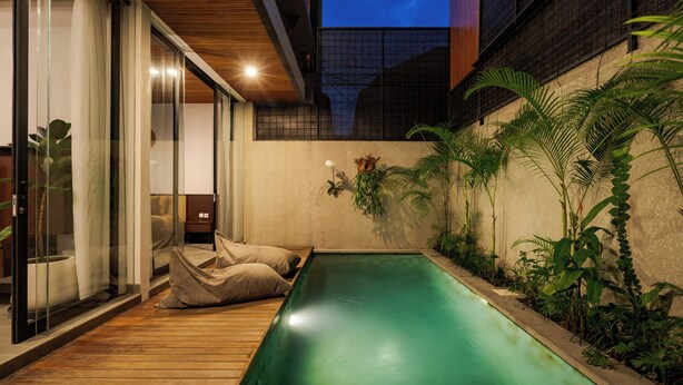 A modern outdoor pool area with a wooden deck, glass doors, and lush greenery. - Aluna Ubud Villas (Ubud)